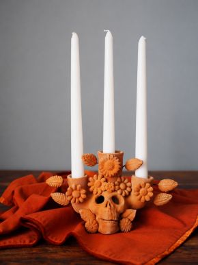 Colorful Día de Muertos altar with marigold garlands, skeleton figures, decorated skulls, candles, food, and portraits.