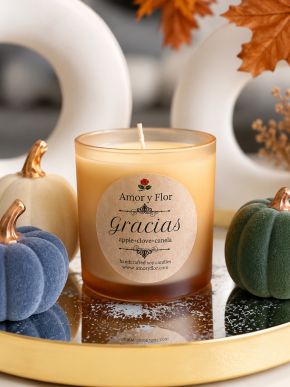 Amber glass soy candle with apple, clove, and cinnamon label among decorative pumpkins.