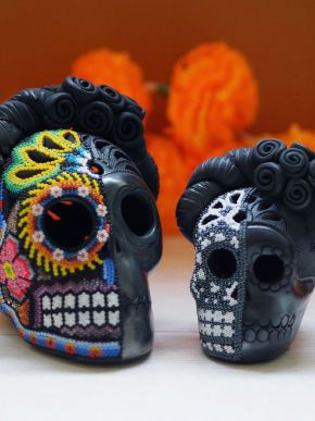 Large multicolored beaded skull and smaller monochrome skull displayed before orange marigolds.