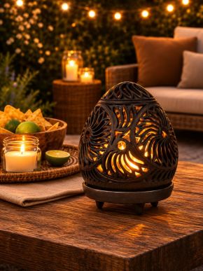 Black carved candle holder glowing on a wooden table in a warm outdoor setting.