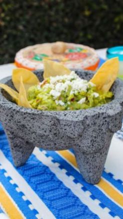 Gray volcanic stone molcajete filled with guacamole, tortilla chips, and crumbled cheese outdoors.