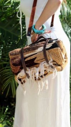 Lifestyle photo of a woven picnic blanket bag with brown leather straps carried outdoors.
