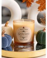 Amber glass soy candle with apple, clove, and cinnamon label among decorative pumpkins.