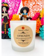 White glass Ofrenda soy candle with copal and sandalwood label before colorful Día de Muertos decorations.