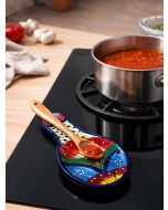 Painted ceramic spoon rest holding a salsa-covered wooden spoon beside a simmering saucepan.