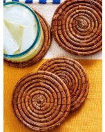 Overhead view of four handwoven pine needle coasters with a blue-rimmed drink on one.