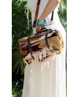 Lifestyle photo of a woven picnic blanket bag with brown leather straps carried outdoors.