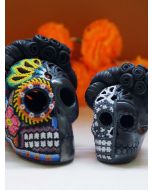 Large multicolored beaded skull and smaller monochrome skull displayed before orange marigolds.